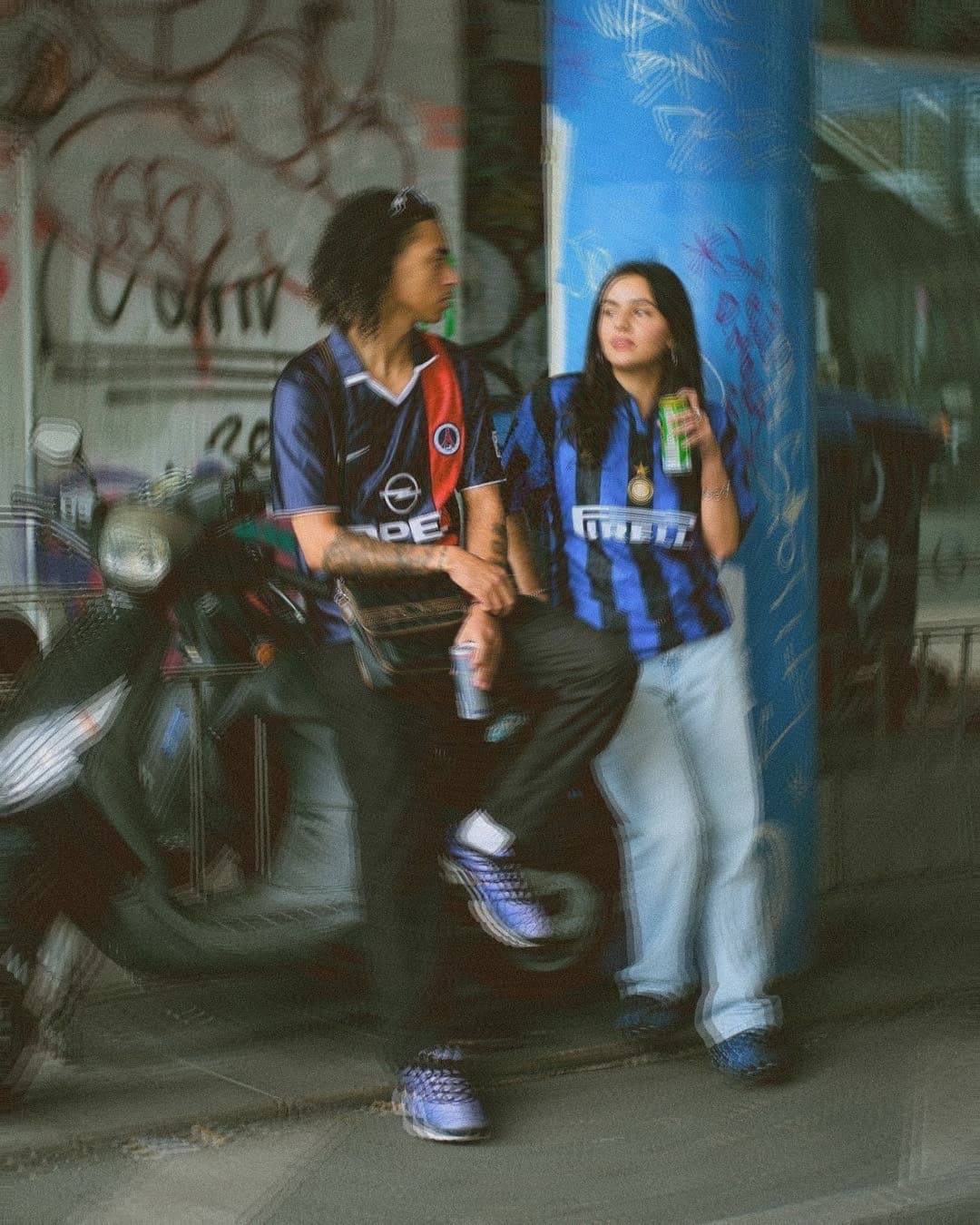 Mujer y varón sentados en una moto vestidos con camisertas de fútbol retros
