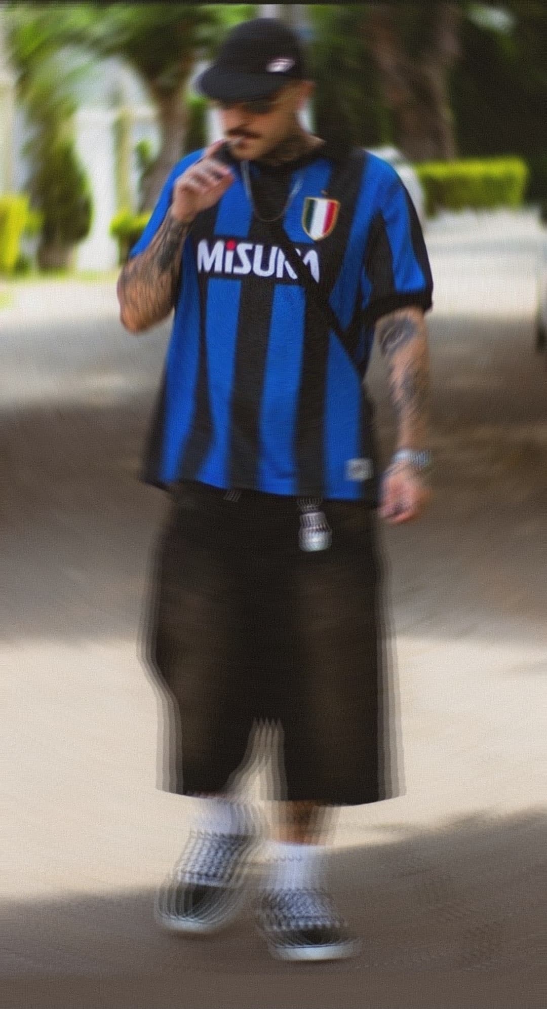 Tipo con estilo caminando y fumando mientras se viste con una prenda de fútbol con estilo Blokecore predominante en su outfit